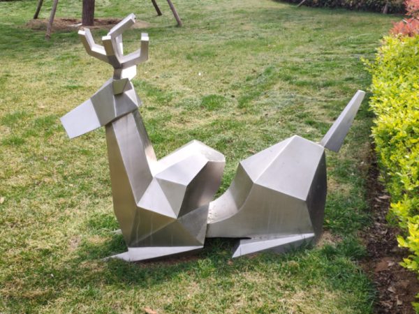 Stainless steel sheep sculpture lying on the green land of the park