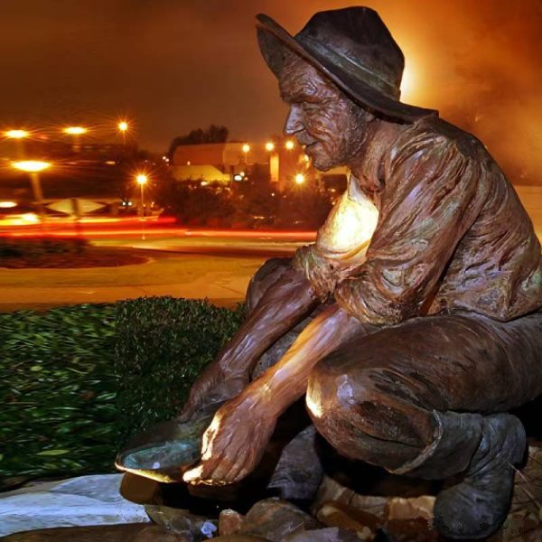 Bronze statue of an old man wearing a beret, rolled up sleeves, and short boots, squatting on the street pouring water with a basin - Image 4