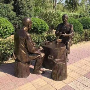 Bronze statue of two male old men sitting on a pole with teapots and cups, drinking tea in a park street