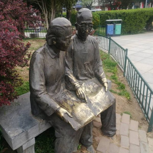 Bronze sculpture in an outdoor park showing two elderly people sitting side by side on a stone bench - Image 2