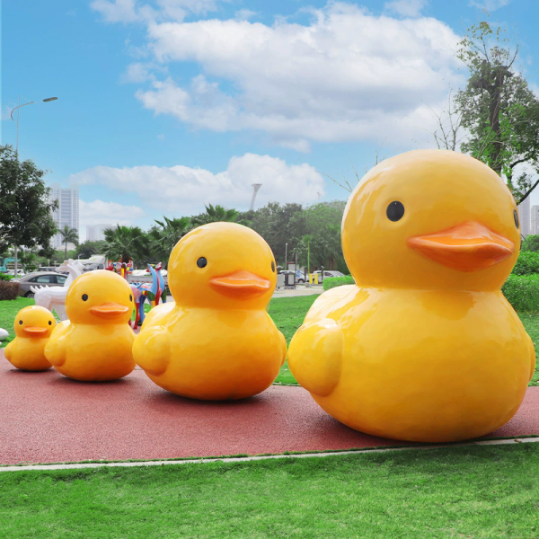 A fiberglass reinforced plastic sculpture of a small yellow duck in an outdoor park public area - Image 4