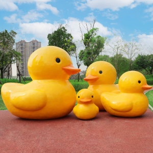 A fiberglass reinforced plastic sculpture of a small yellow duck in an outdoor park public area