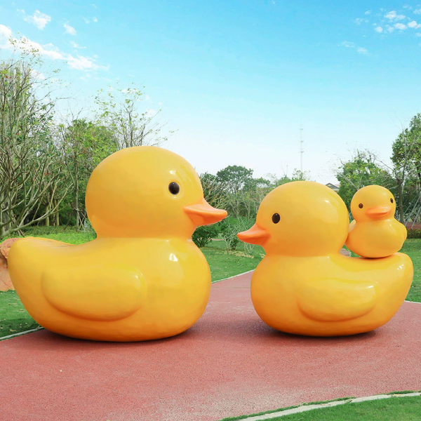 A fiberglass reinforced plastic sculpture of a small yellow duck in an outdoor park public area - Image 3