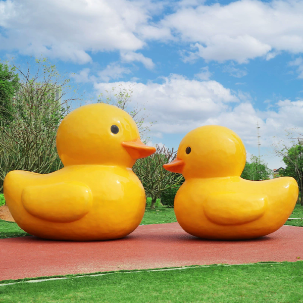 A fiberglass reinforced plastic sculpture of a small yellow duck in an outdoor park public area - Image 2